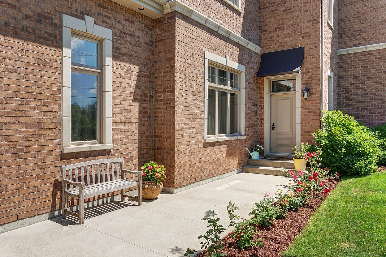 Brick home exterior with landscaped front walkway, garden bed, and small entry porch.