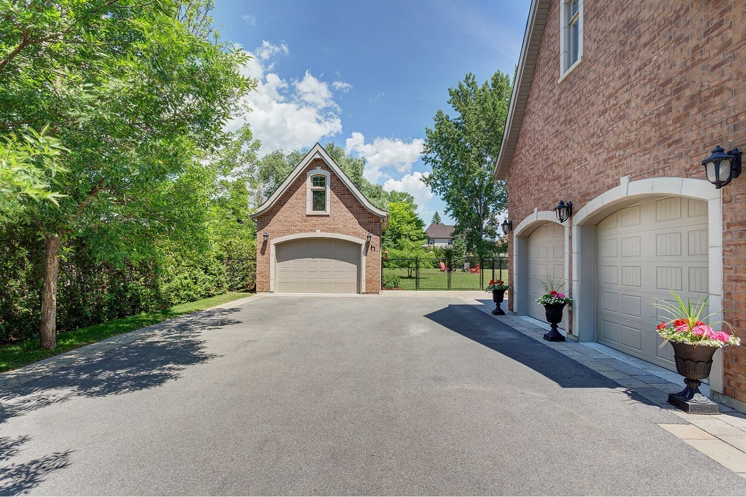 Large paved driveway featuring attached double garage and separate brick garage surrounded by greenery.