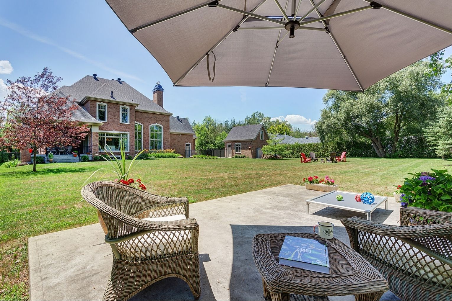 Spacious backyard with patio seating, large lawn, and brick home with detached garage.