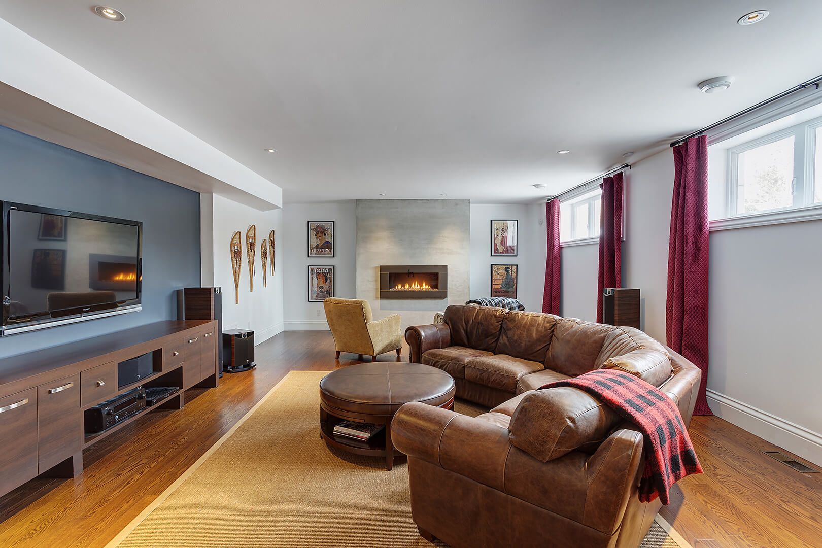 Finished basement with leather sectional sofa, wall-mounted TV, and modern gas fireplace.