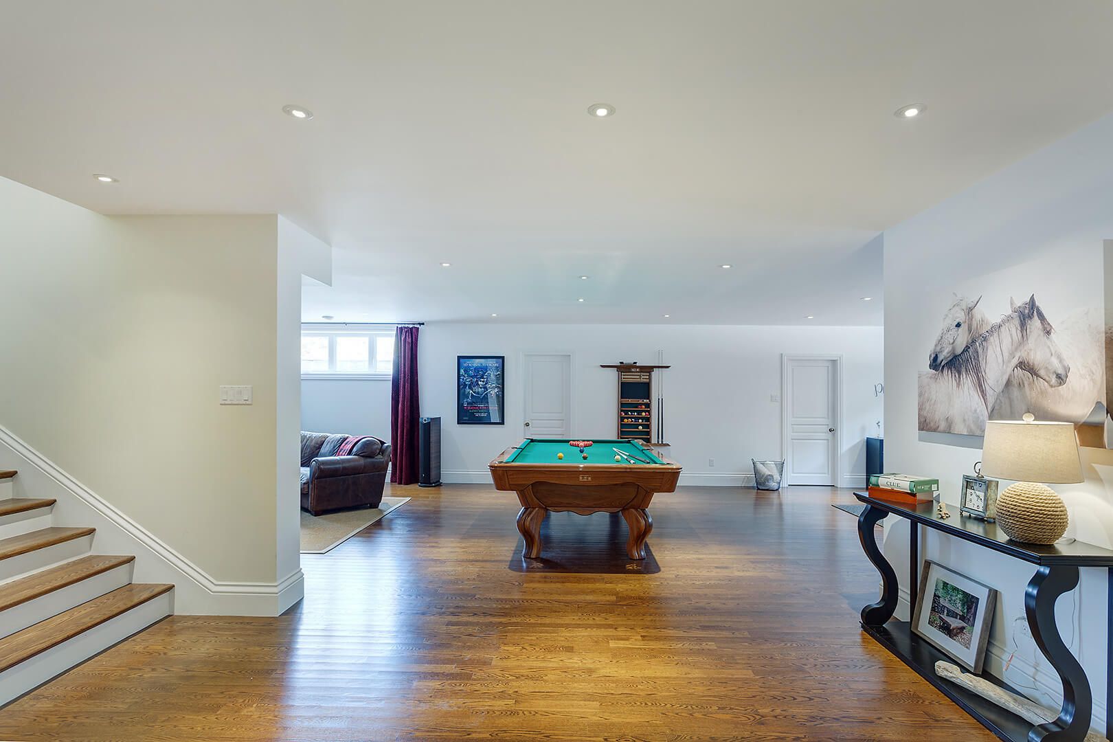 Spacious finished basement featuring a billiards table, lounge area, and hardwood floors.