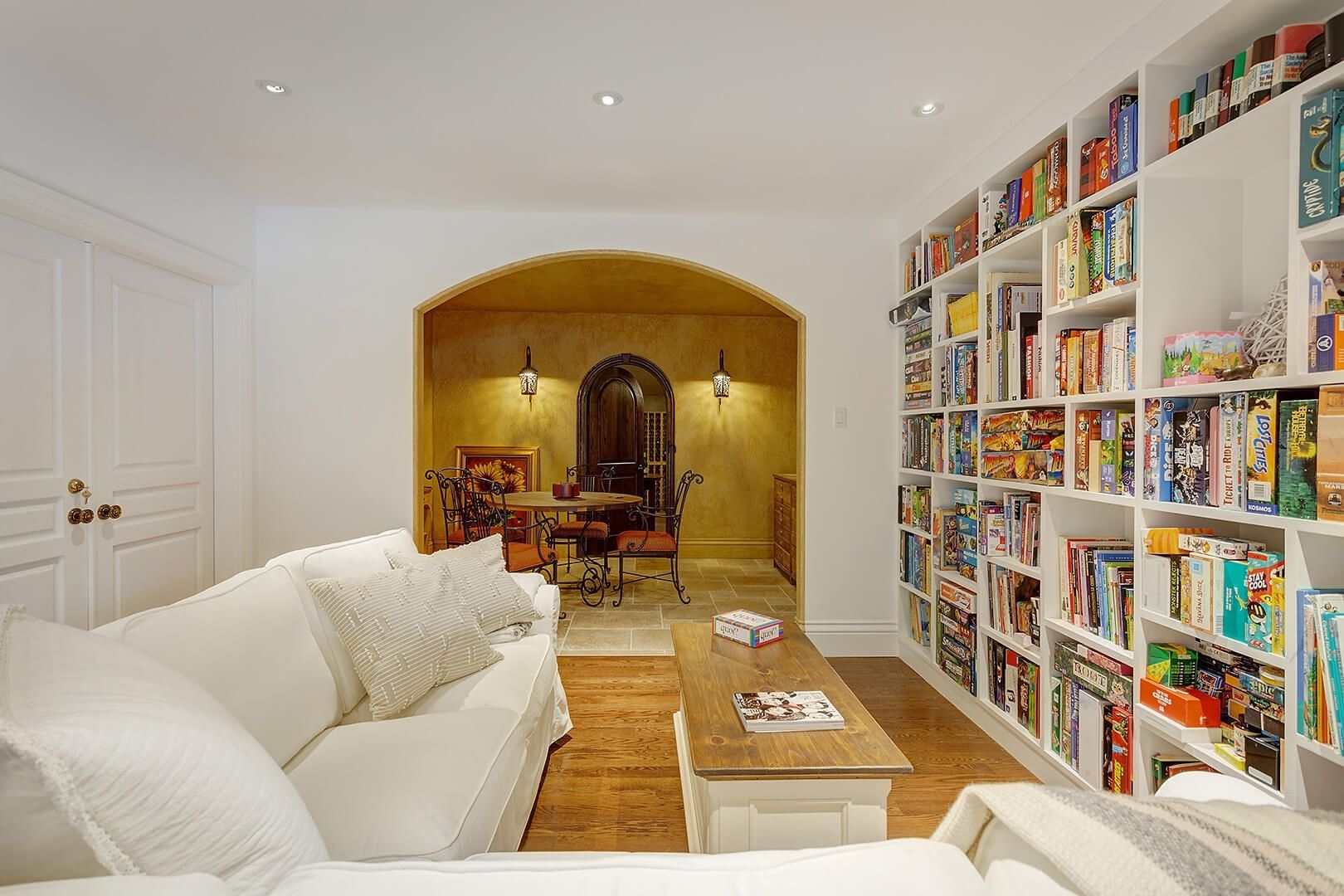 Finished basement featuring a white sectional sofa, built-in game shelf, and arched entryway to a wine cellar.