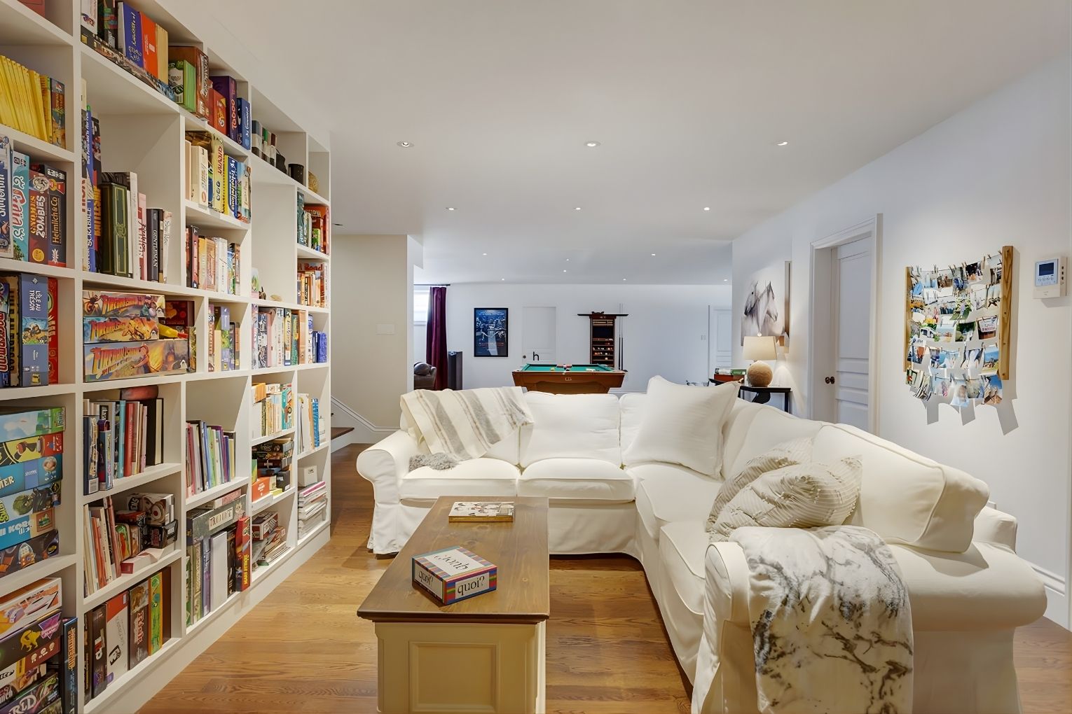 Finished basement with white sectional sofa, board-game shelving, and pool table in background.