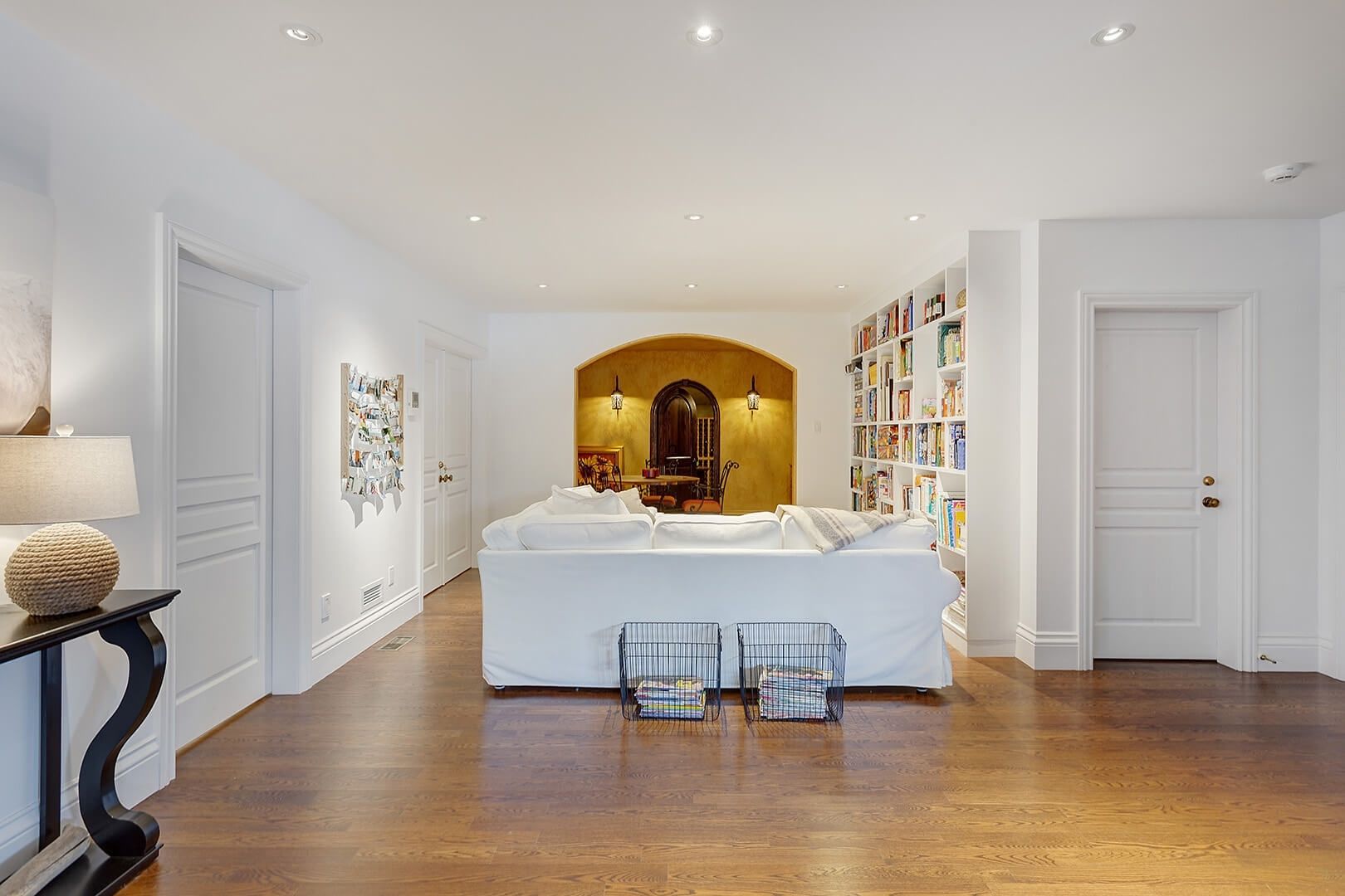 Finished basement with white sectional sofa, large built-in bookshelf, and arched doorway to wine cellar.