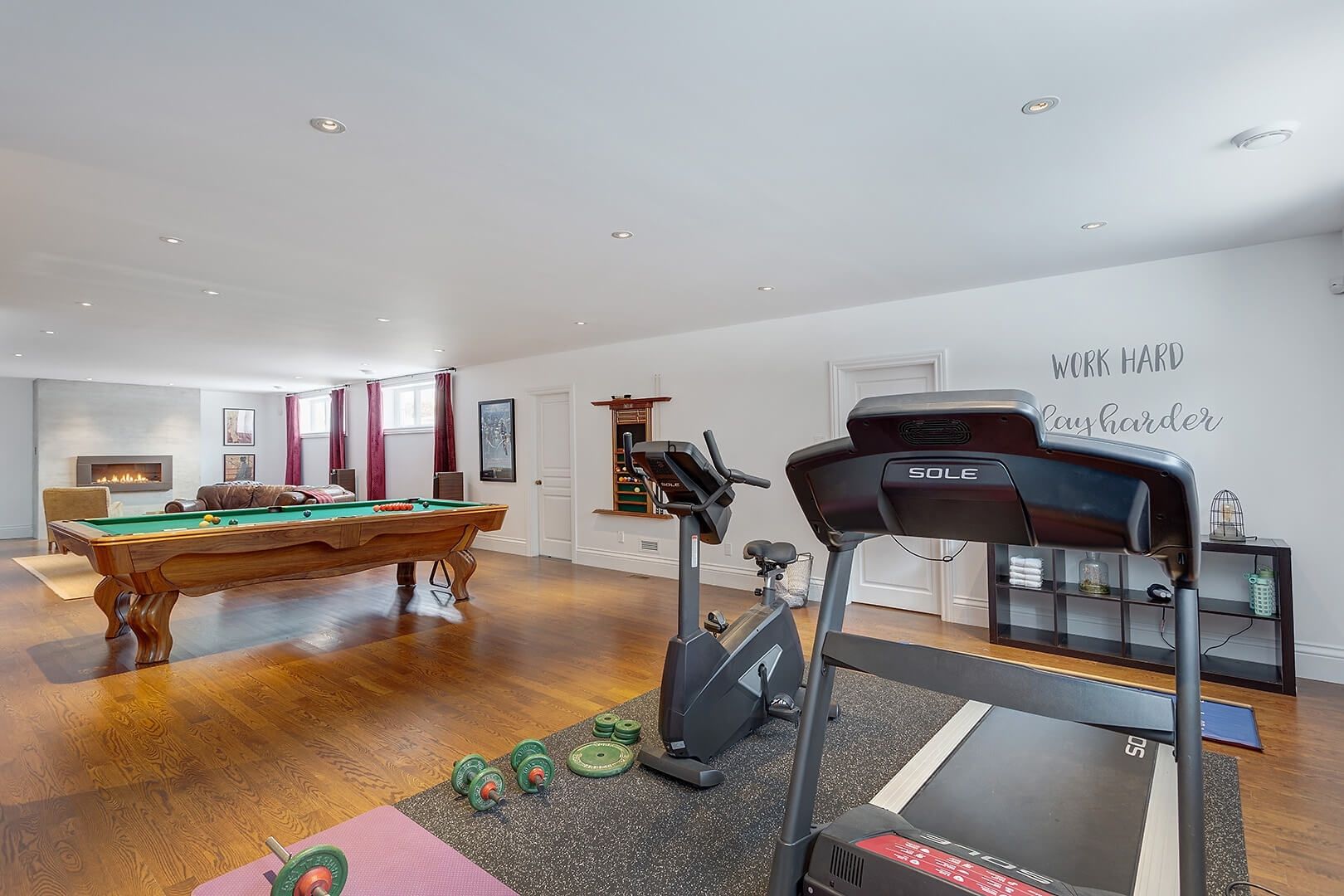 Open-concept finished basement with home gym equipment and a pool table.